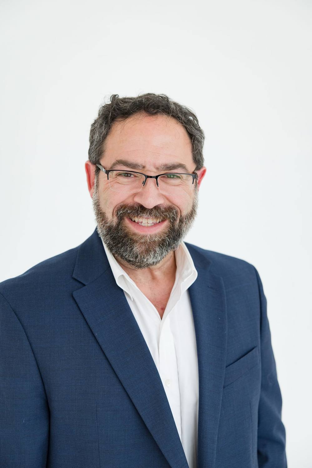 Jeff Green, head and shoulders, smiling in a navy blazer and glasses against a white backdrop